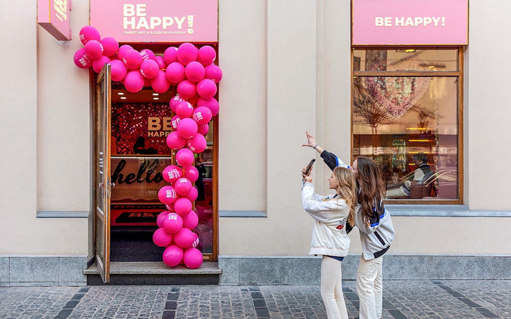 Entrance to Be Happy Museum in Krakow with pink balloon arch and visitors taking photos.