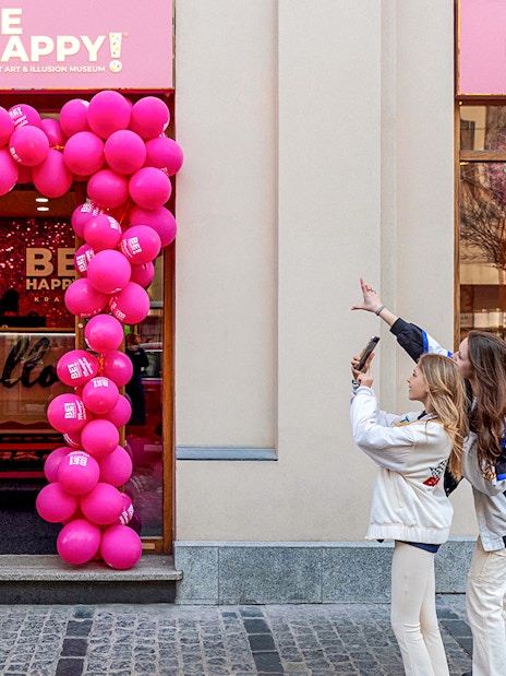 Entrance to Be Happy Museum in Krakow with pink balloon arch and visitors taking photos.