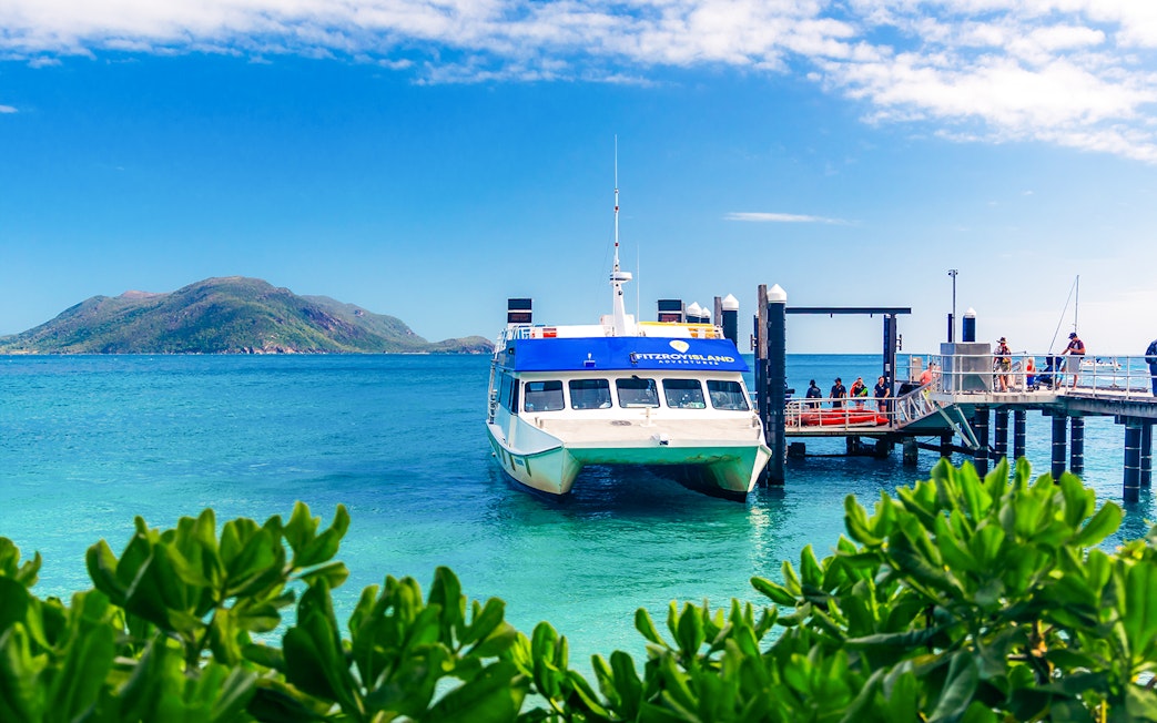 Ferry docked at Fitzroy Island pier with lush greenery and ocean view, Cairns half-day cruise.