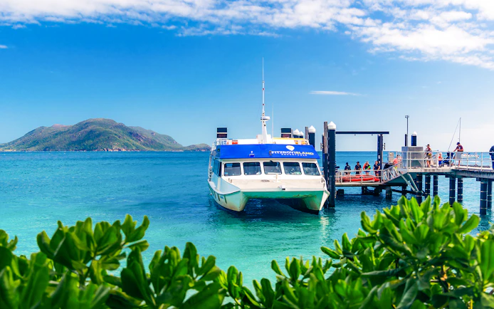Ferry docked at Fitzroy Island pier with lush greenery and ocean view, Cairns half-day cruise.