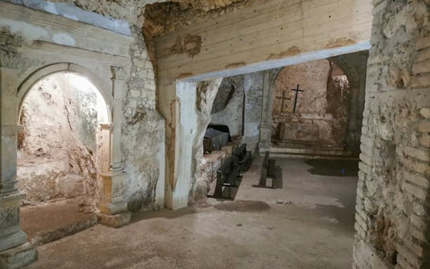 Underground chamber with stone arches and benches in Cagliari, featuring ancient crosses.