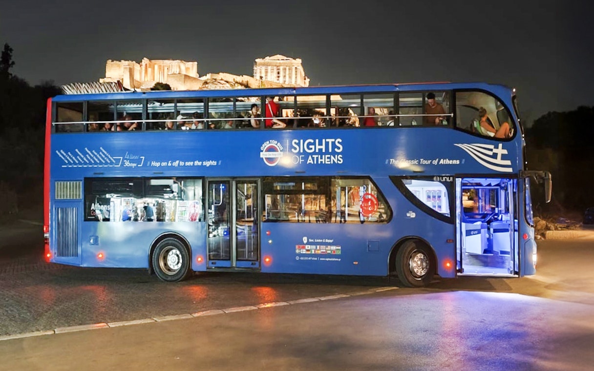 Open double-decker bus in Athens with Acropolis view at night.