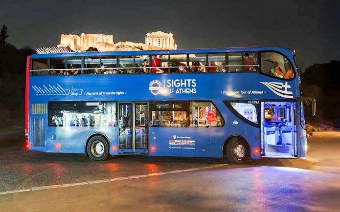 Open double-decker bus in Athens with Acropolis view at night.
