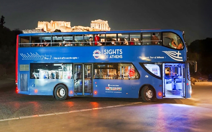 Open double-decker bus in Athens with Acropolis view at night.