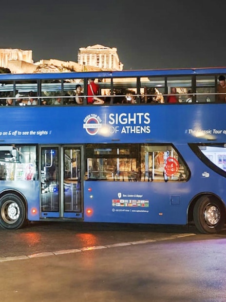 Open double-decker bus in Athens with Acropolis view at night.