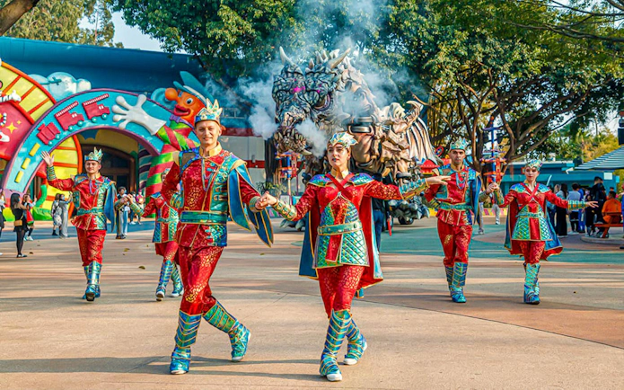 Performers in colorful costumes at Chimelong Paradise with dragon float in background.