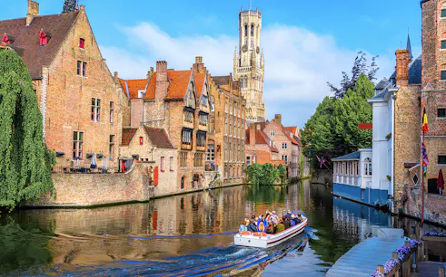 Boat tour on Bruges canal with Belfry of Bruges in background, Belgium.