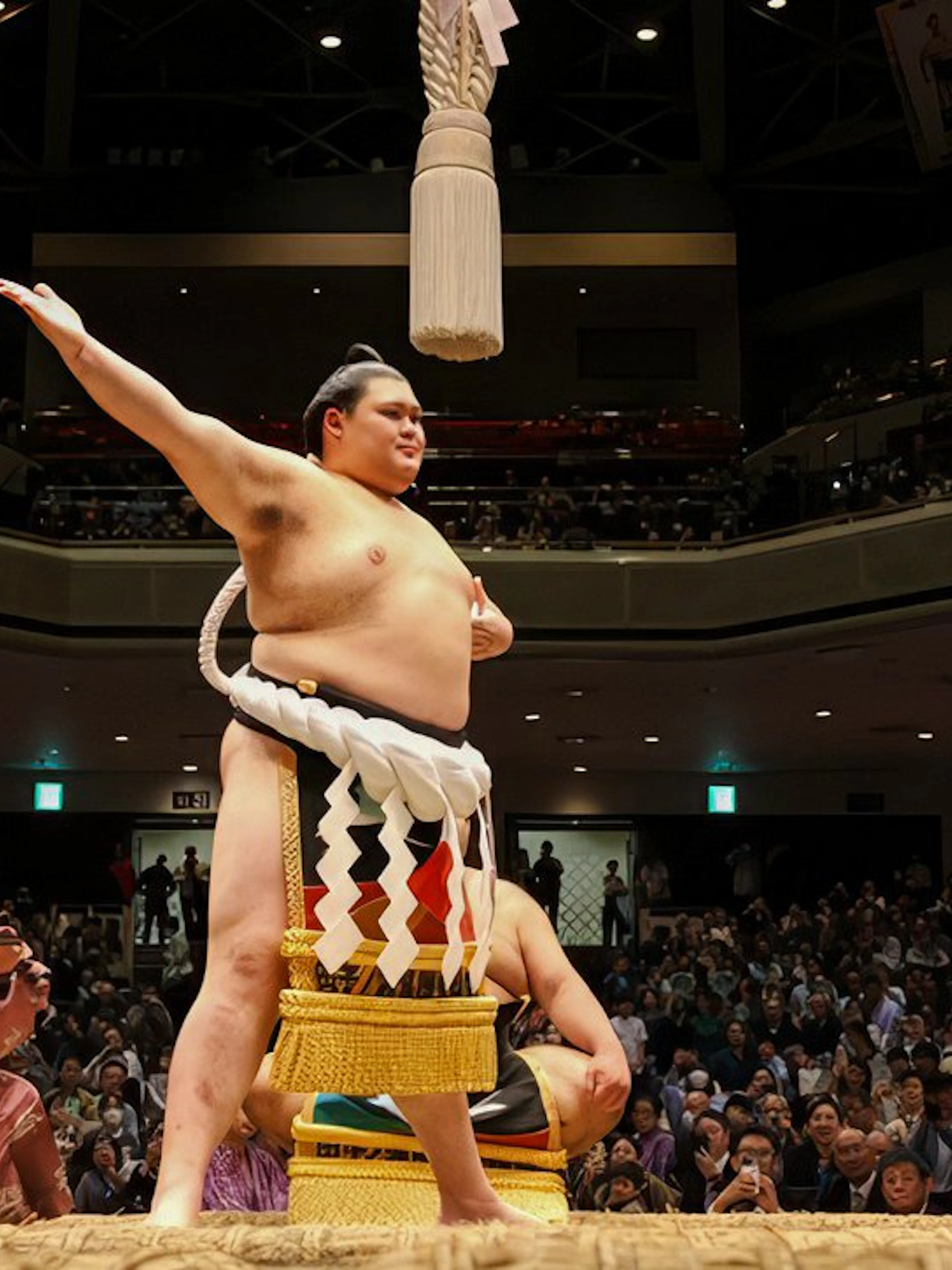 Sumo wrestler celebrating in a packed arena in Japan.