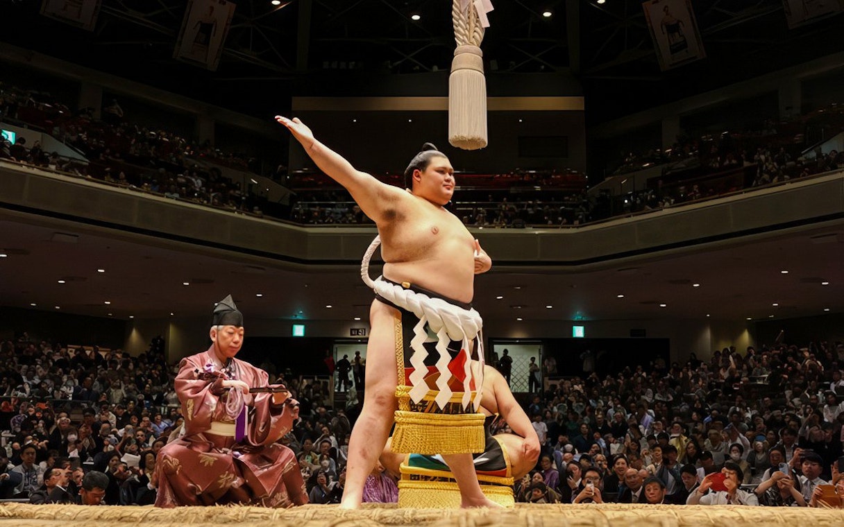 Sumo wrestler celebrating in a packed arena in Japan.