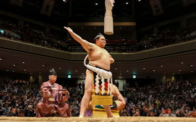 Sumo wrestler celebrating in a packed arena in Japan.