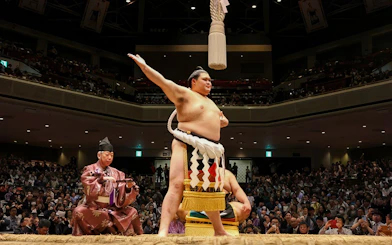 Sumo wrestler celebrating in a packed arena in Japan.