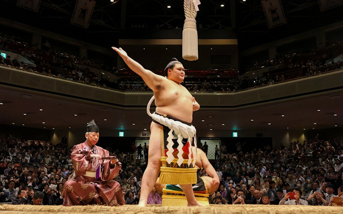 Sumo wrestler celebrating in a packed arena in Japan.