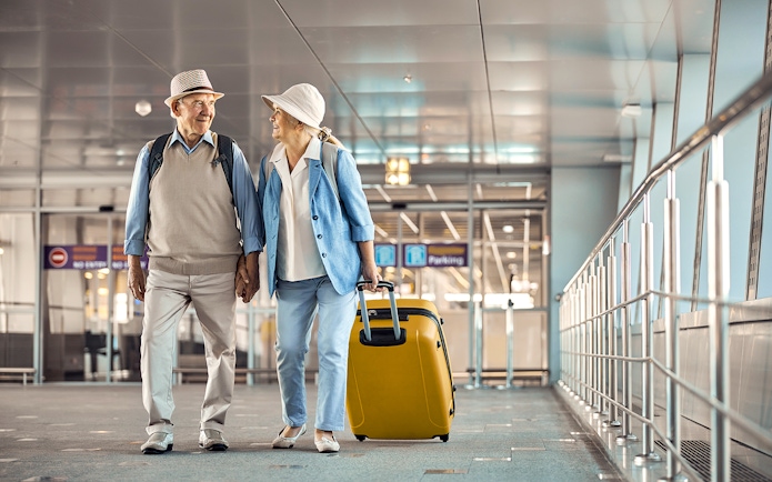 Senior couple with luggage walking through Heathrow airport terminal.