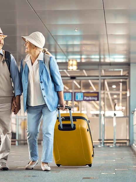 Senior couple with luggage walking through Heathrow airport terminal.