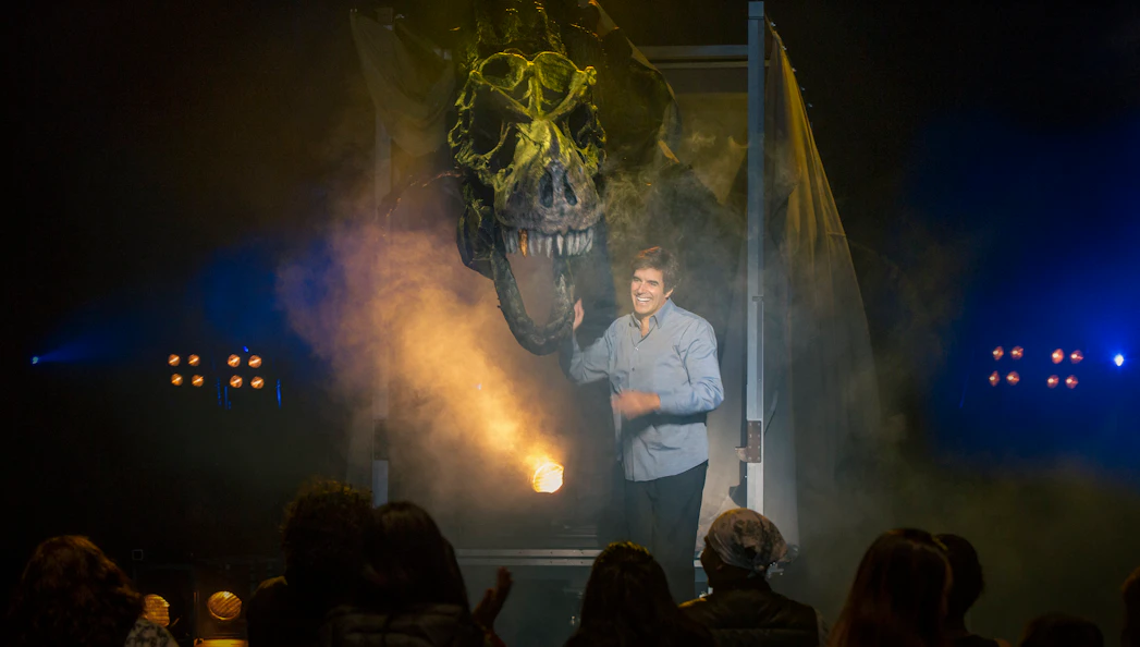 Magician on stage with dinosaur illusion during Vegas show performance.