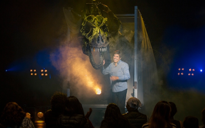 Magician on stage with dinosaur illusion during Vegas show performance.
