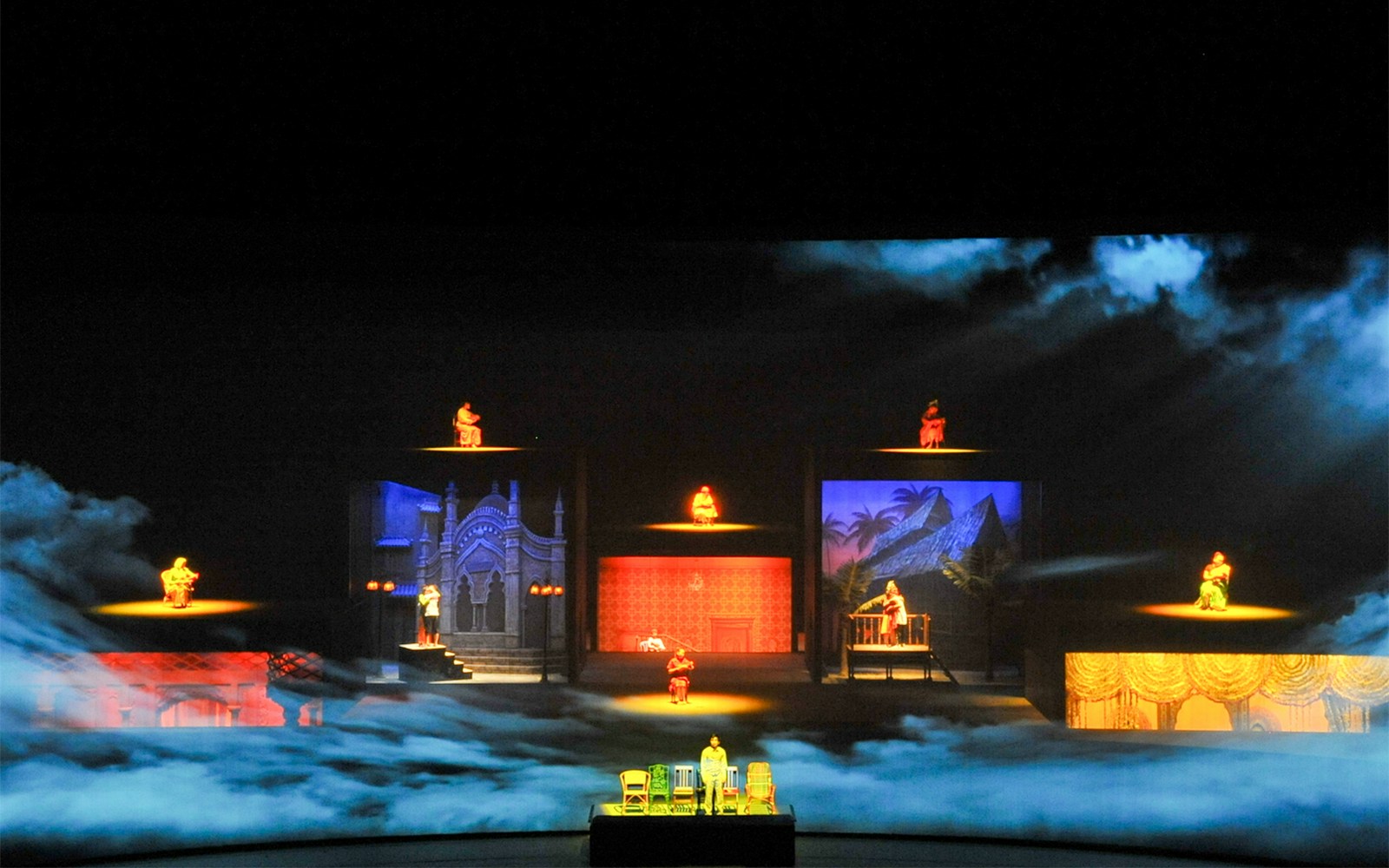 Multi-level stage with performers in colorful attire, showcasing diverse cultural scenes.