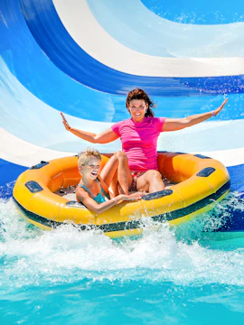 Mother and child on inflatable raft sliding down waterpark slide.