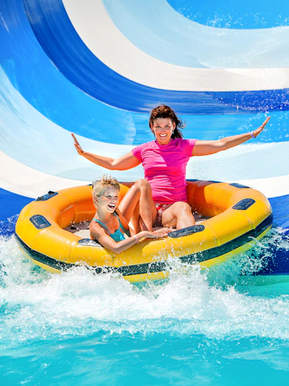 Mother and child on inflatable raft sliding down waterpark slide.