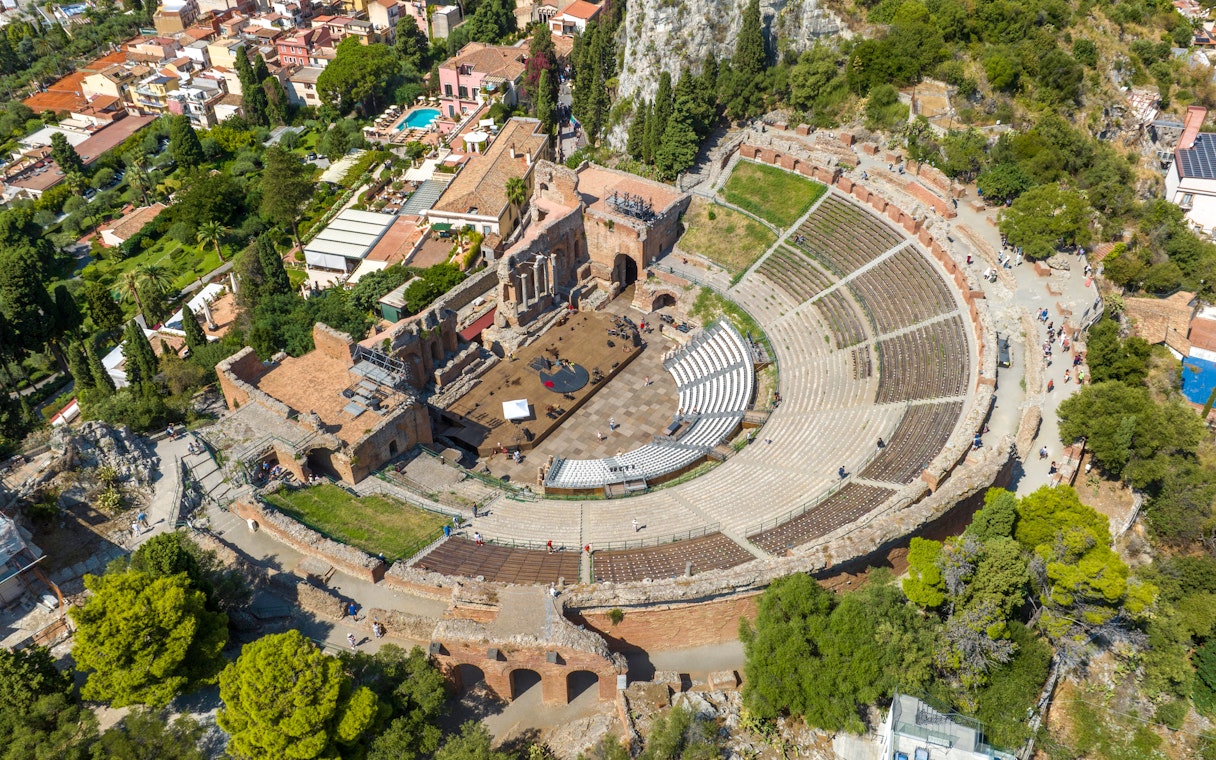Aerial view of the ancient theatre of Taormina, surrounded by greenery and buildings, Sicily, Italy.