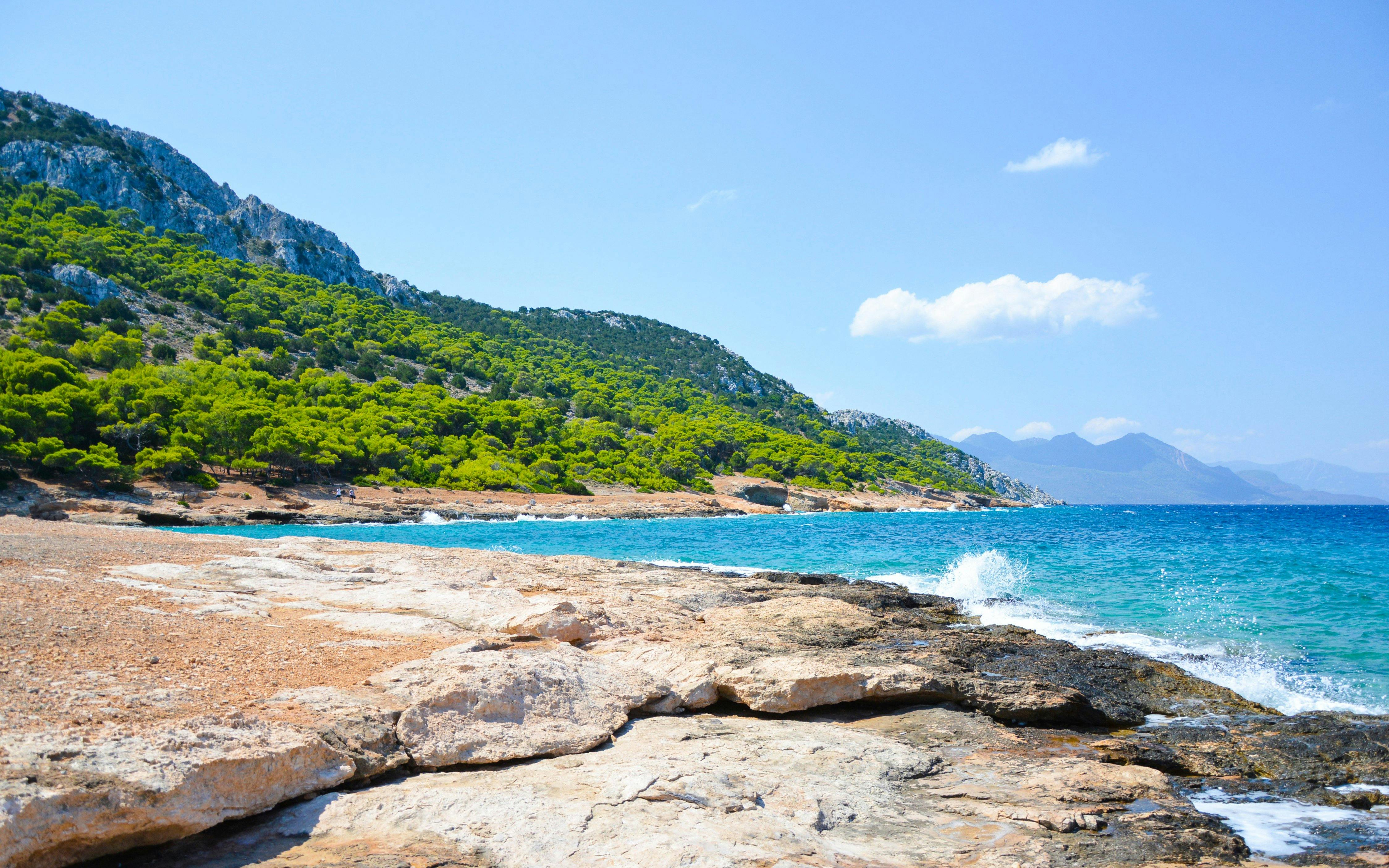Rocky coastline with turquoise waters and lush greenery on Moni Island, Greece.