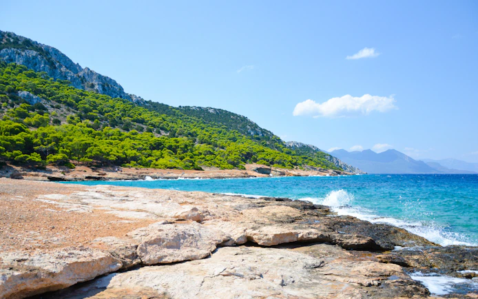 Rocky coastline with turquoise waters and lush greenery on Moni Island, Greece.