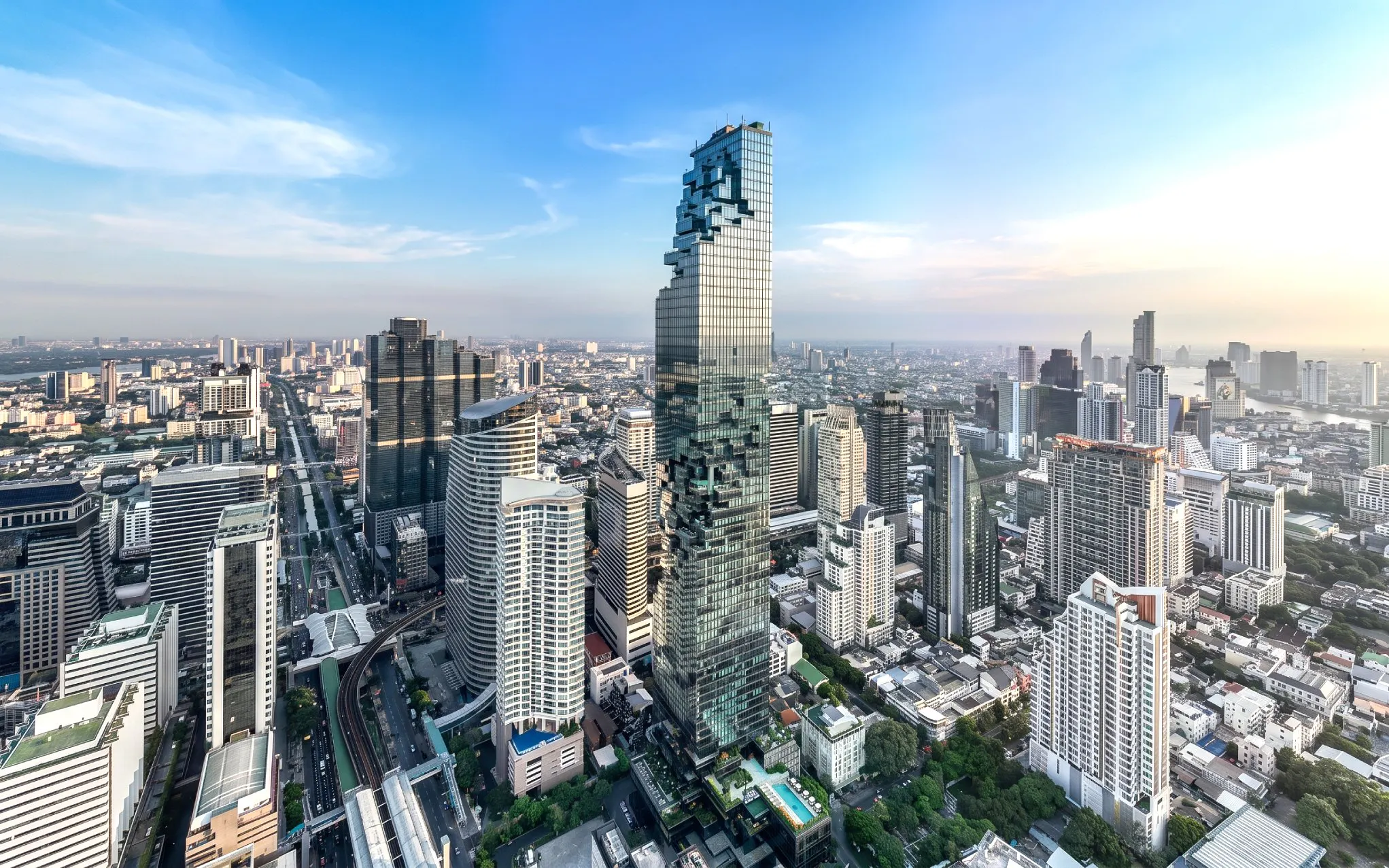 High-angle view of King Power Mahanakhon skyscraper in Bangkok cityscape under clear blue sky.