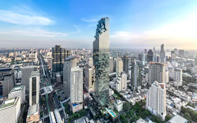 High-angle view of King Power Mahanakhon skyscraper in Bangkok cityscape under clear blue sky.