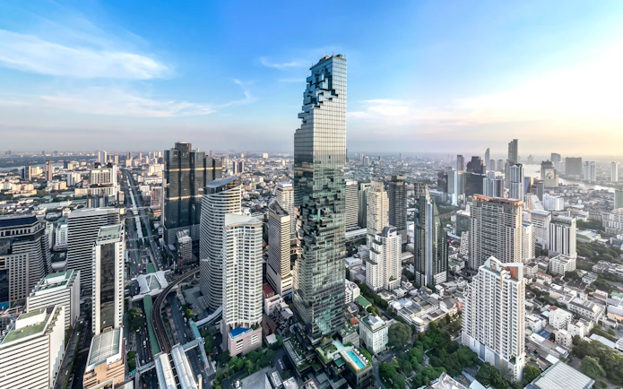 High-angle view of King Power Mahanakhon skyscraper in Bangkok cityscape under clear blue sky.