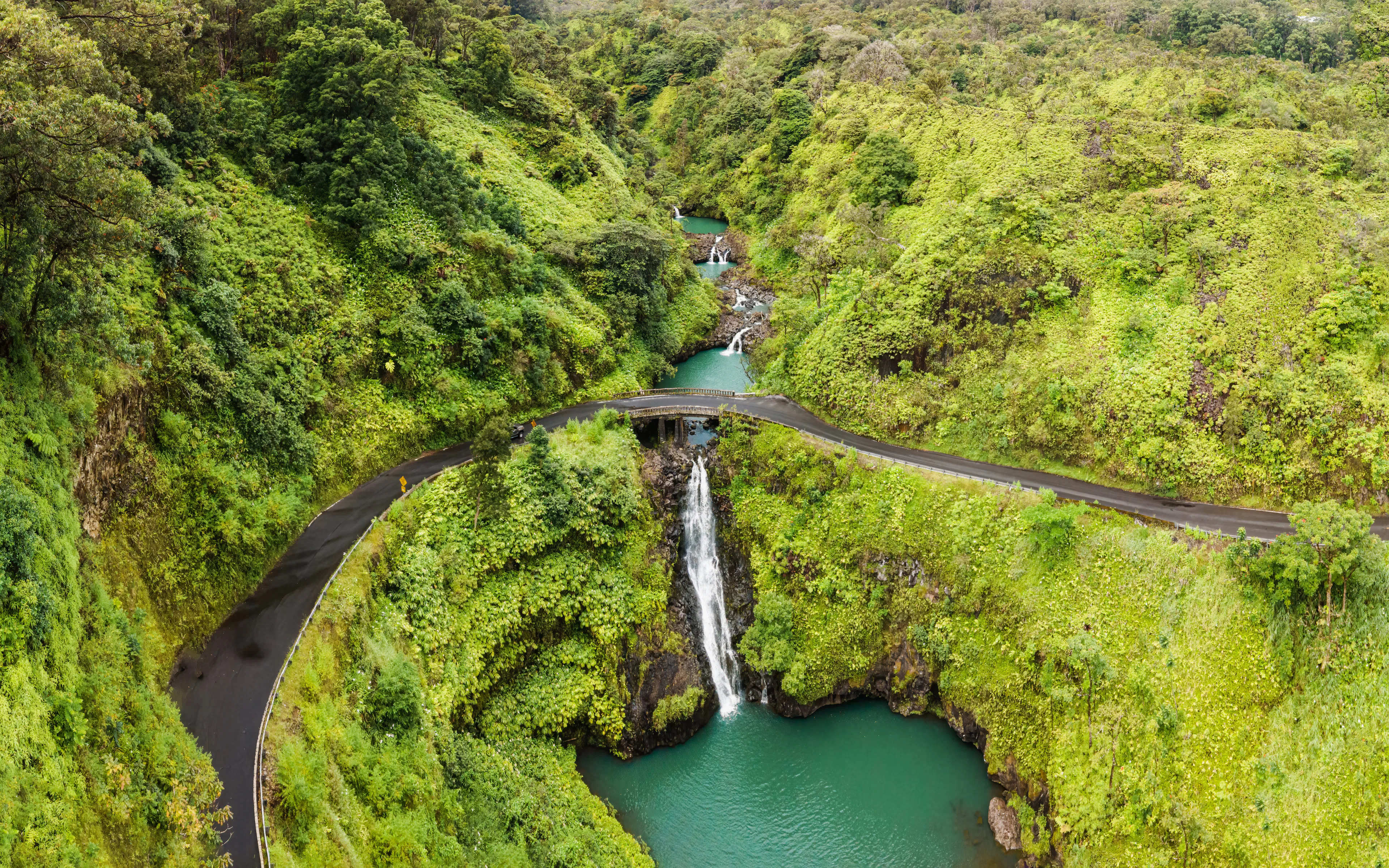 Aerial view of Maui waterfalls and bridge on the road to Hana, surrounded by lush greenery.