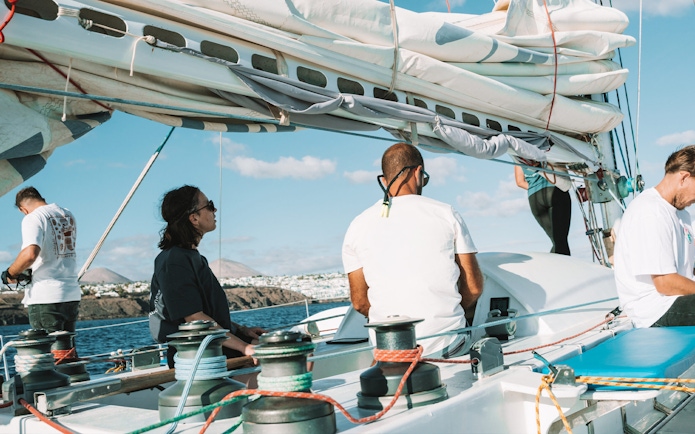 Tourists on a private sailboat tour for dolphin watching near coastal cliffs.