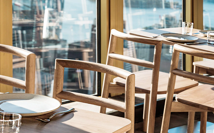 Dining setup with wooden chairs and table at SkyFeast, Sydney Tower, overlooking cityscape.