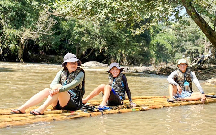 Three people bamboo rafting on a river surrounded by lush greenery.