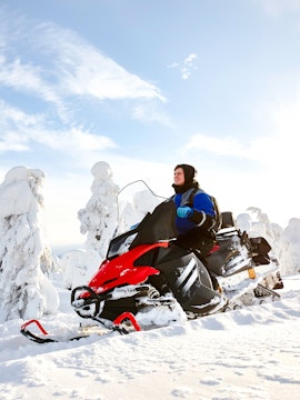 Man driving snowmobile through snowy landscape in Lapland.