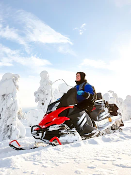 Man driving snowmobile through snowy landscape in Lapland.