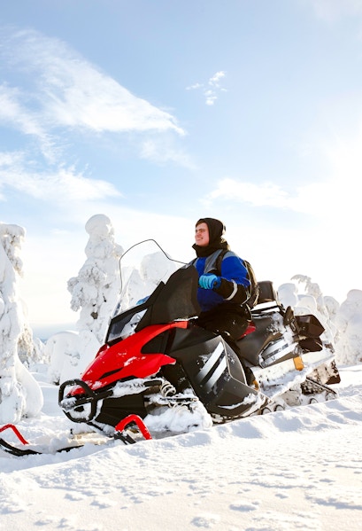 Man driving snowmobile through snowy landscape in Lapland.