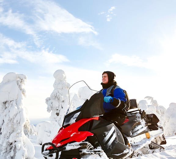 Man driving snowmobile through snowy landscape in Lapland.