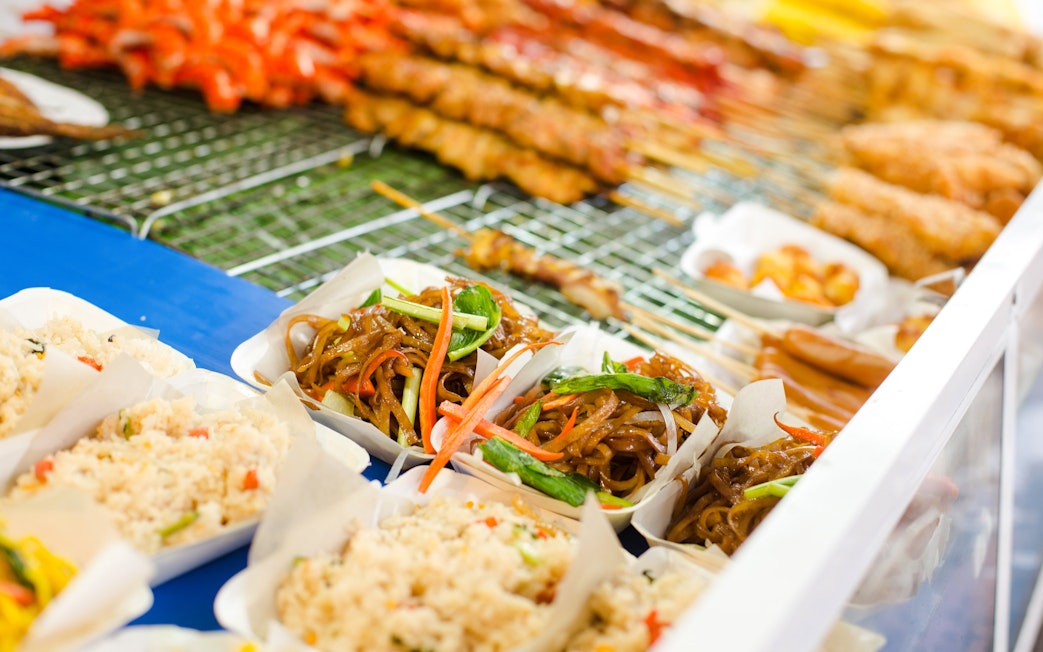 Thai street food with noodles, rice, and skewers on display.