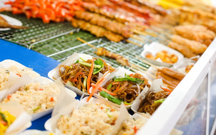 Thai street food with noodles, rice, and skewers on display.