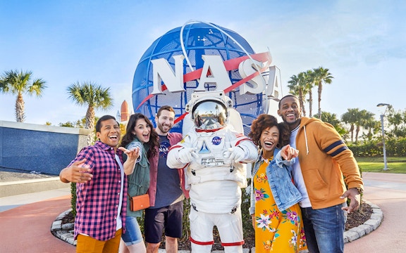 Visitors posing with astronaut in front of NASA globe at Kennedy Space Center, Florida.