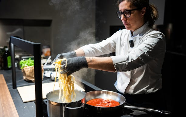 Chef preparing pasta in a Rome cooking class with boiling water and tomato sauce.