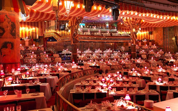Dinner seating arrangement at Moulin Rouge with red lamps and tiered tables.