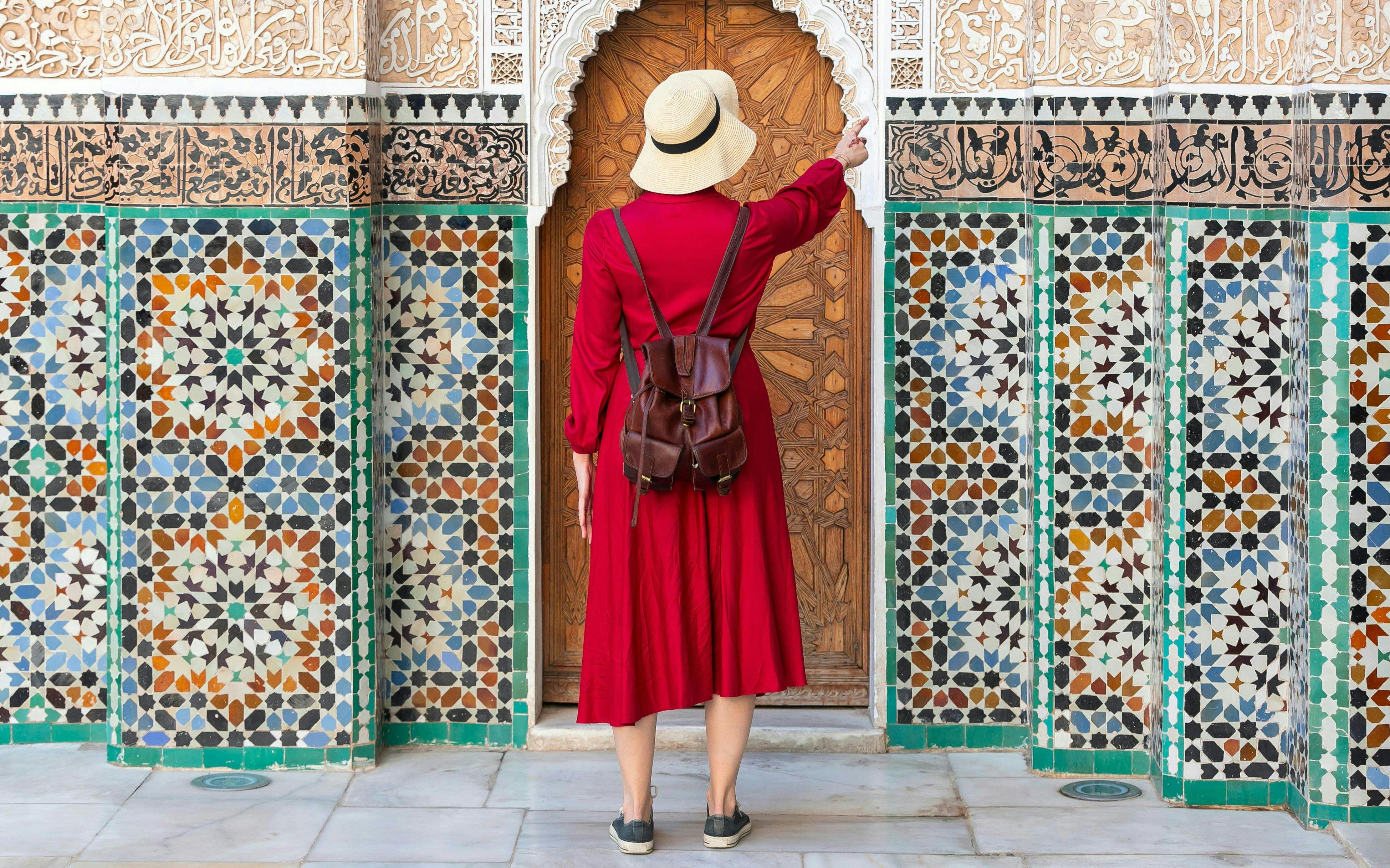 Girl in red dress and hat admiring Ben Youssef Madrasa tiles, Marrakech, Morocco.