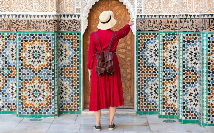 Girl in red dress and hat admiring Ben Youssef Madrasa tiles, Marrakech, Morocco.