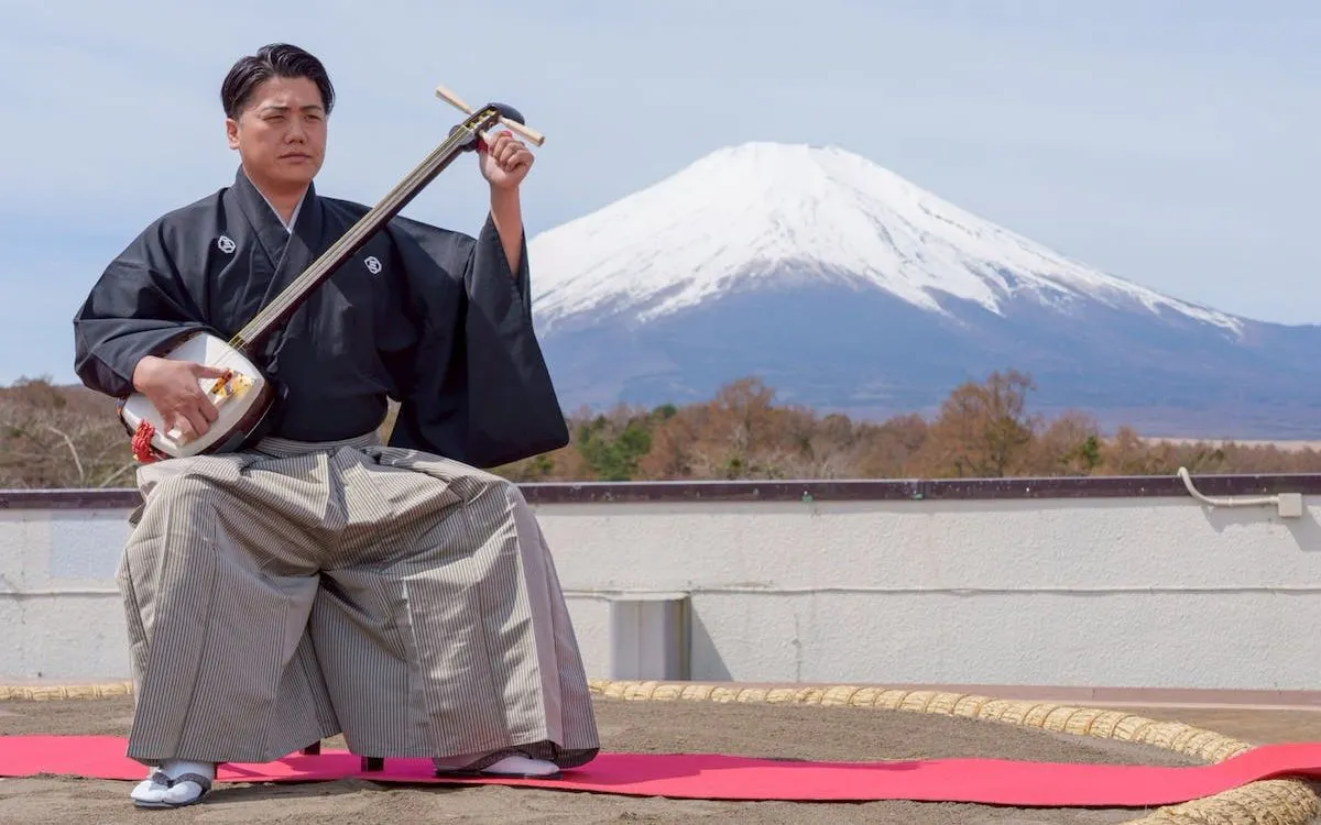 Sumo wrestler playing shamisen with Mount Fuji in the background, Yamanashi.