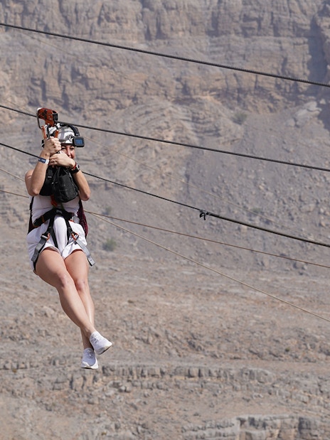 Person ziplining at Jebel Jais, Ras Al Khaimah, with rocky mountain backdrop.