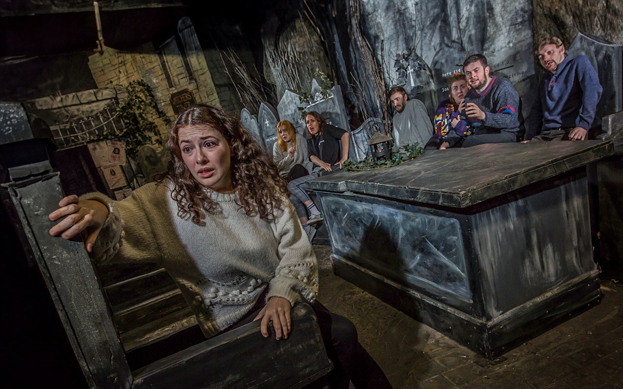 Tourists experiencing the eerie Kirkyard scene at The Edinburgh Dungeon in Scotland.
