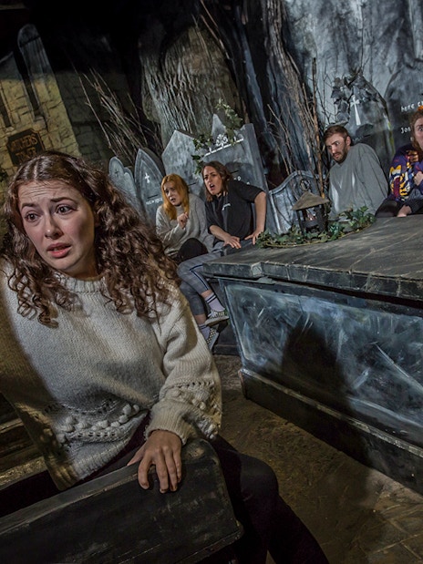 Tourists experiencing the eerie Kirkyard scene at The Edinburgh Dungeon in Scotland.