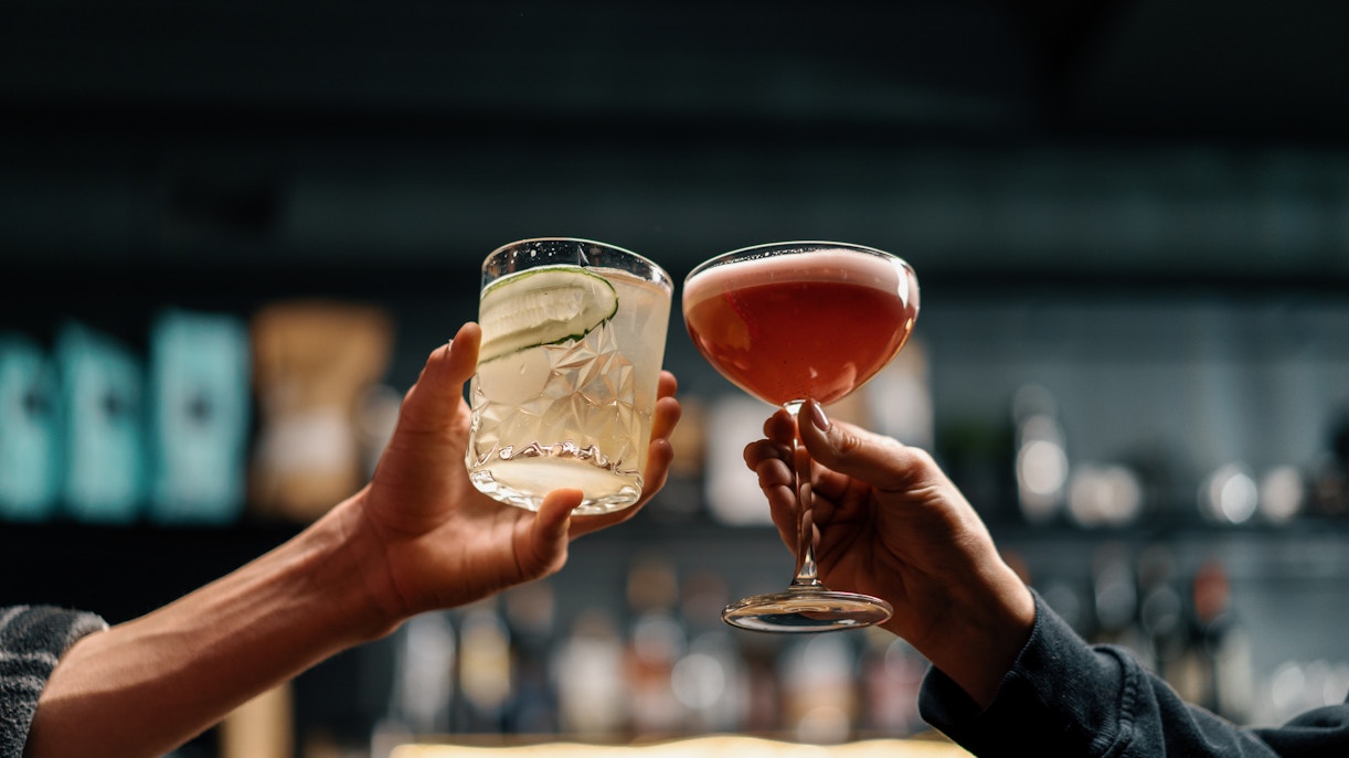 Two people toasting with cocktails in a bar setting.