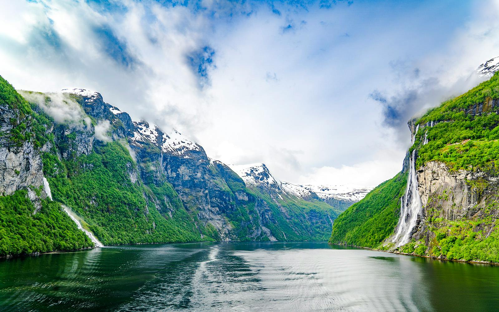 Geirangerfjord in Norway with waterfalls cascading down lush green cliffs.